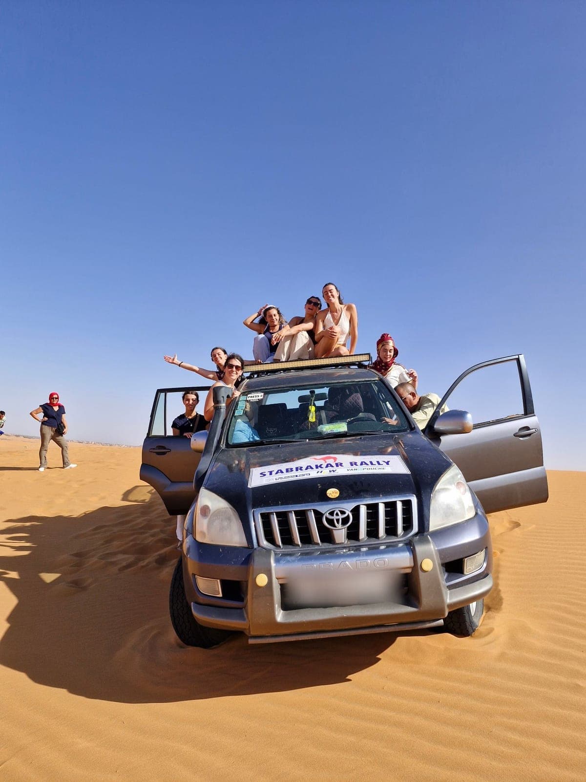 Travellers sitting on top of a four-wheel drive stopped on a golden sand dune