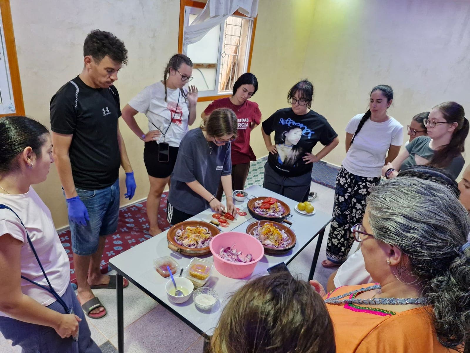 Travellers around a table learning to prepare tagines with onion, tomato and spices